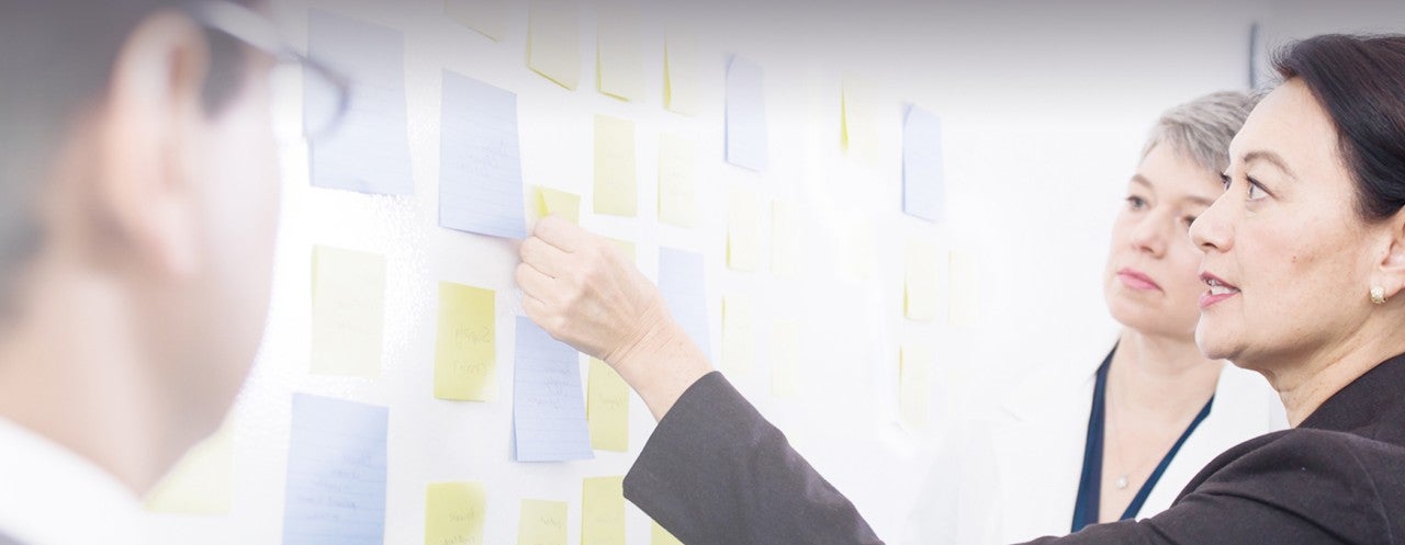 woman in black coat pointing at sticky board