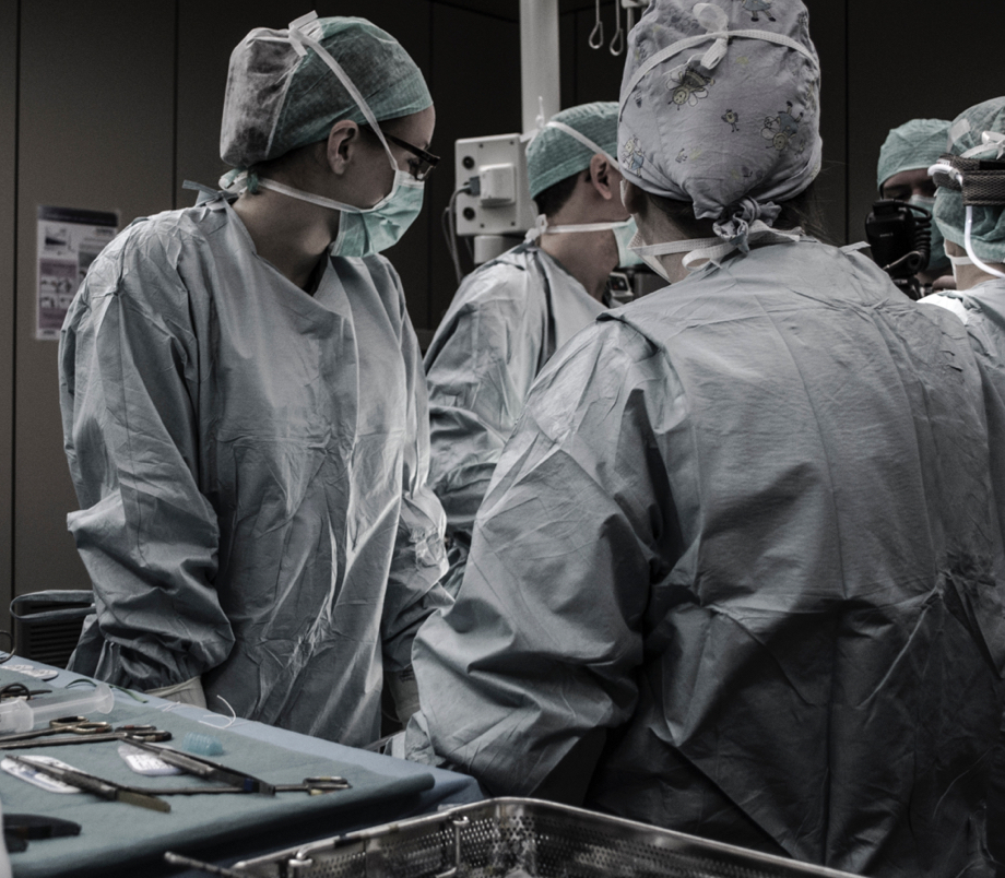 Five people wearing surgical gear, looking in the same direction in an operating room.
