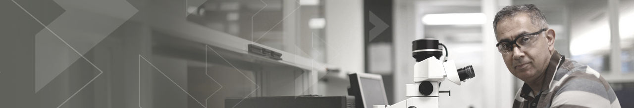 Man with glasses in front of microscope.