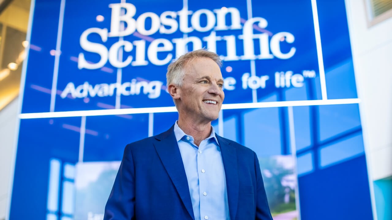 Boston Scientific CEO Mike Mahoney smiling in front of Boston Scientific sign.
