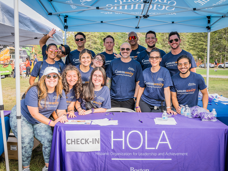 A group of employees in matching blue shirts pose at the check-in tent of a charity walk event.