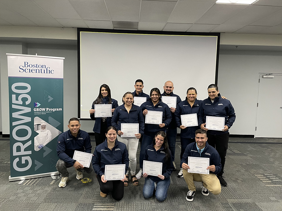 A team of Boston Scientific employees wearing matching navy blue coats hold up their GROW graduation certificates.