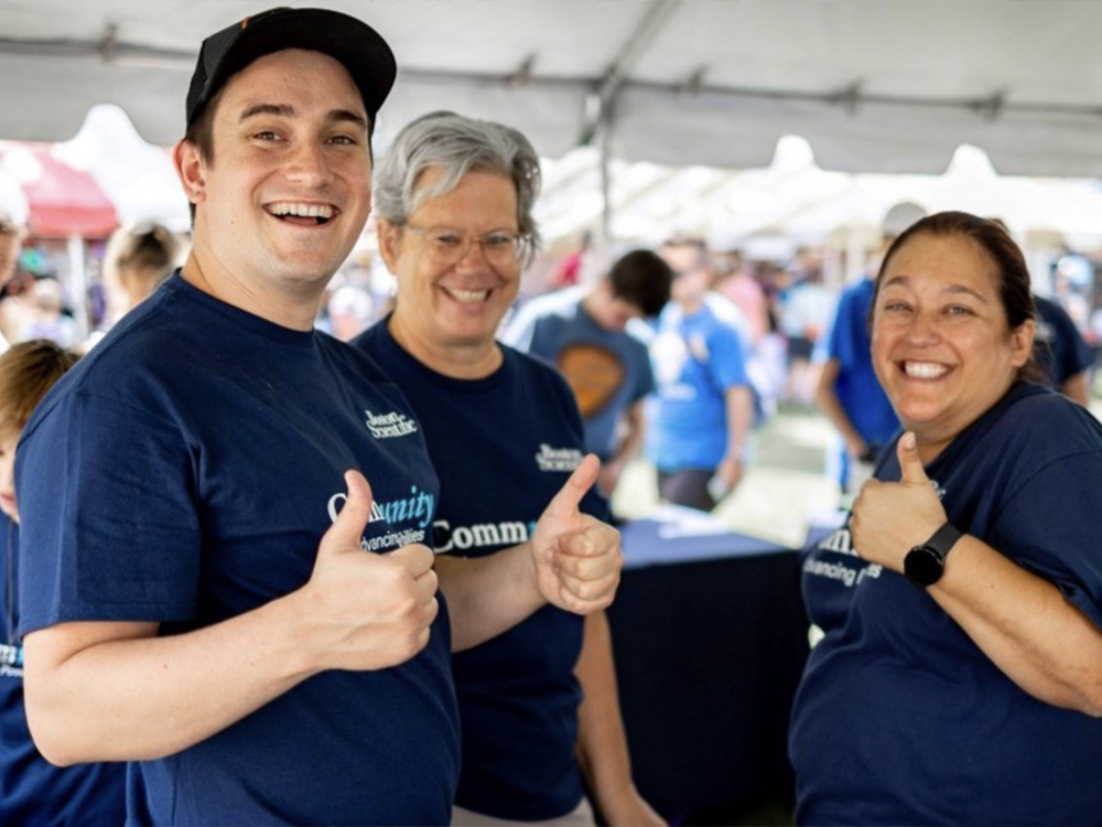 A group of employees in matching blue shirts pose at the check-in tent of a charity walk event.