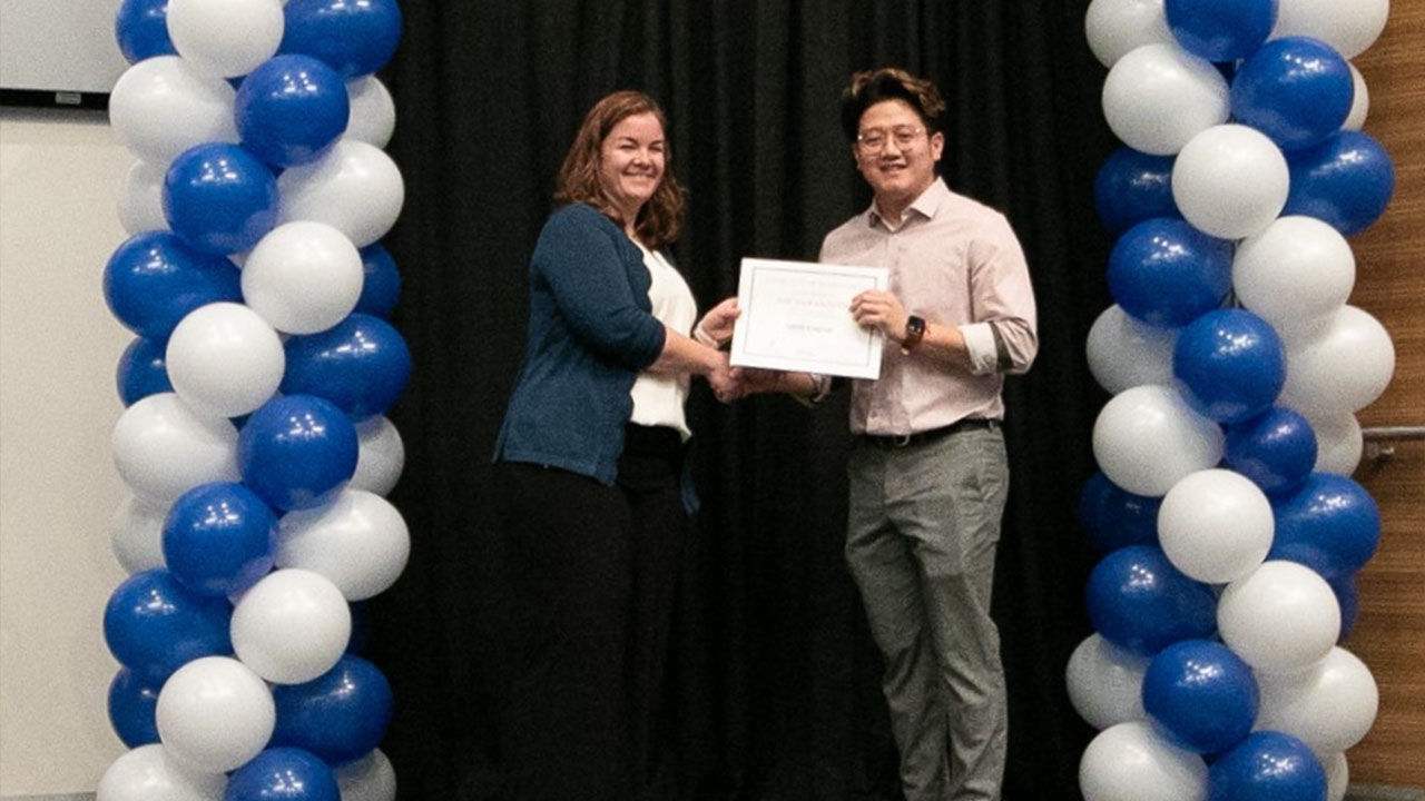 Two smiling woman and a man looking toward camera while holding certificate.