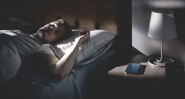 Man sleeping peacefully with smartphone on nightstand.