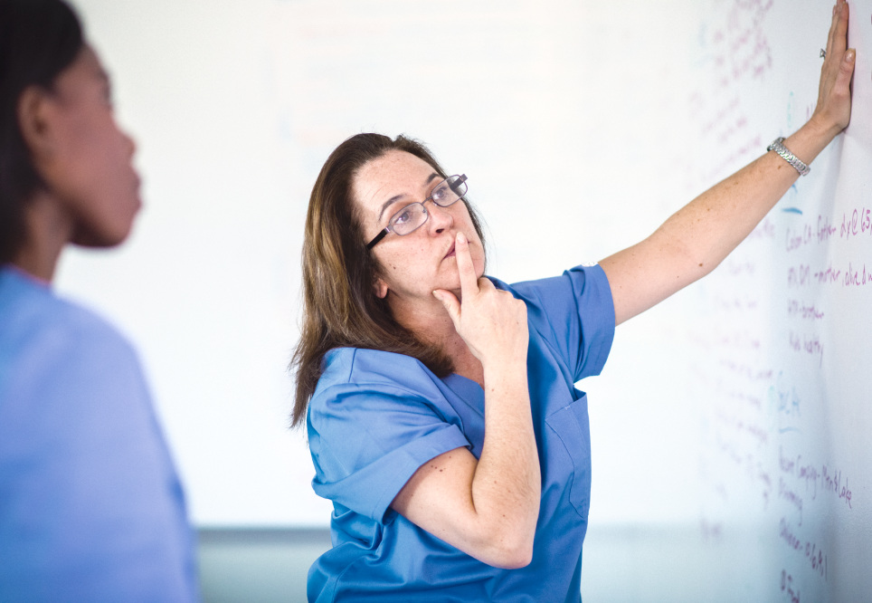 Nurse in blue scrubs leaning one hand on whiteboard