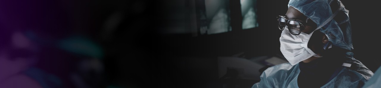 Head and shoulders of gowned physician in lab looking toward unseen monitor.