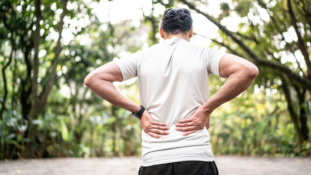 Person outdoors holding lower back with both hands.