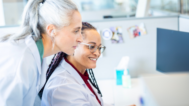 Two health care professionals review information together on a computer in a clinical workspace.