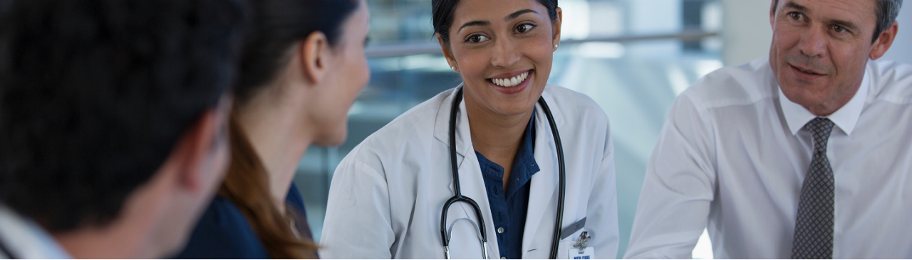 Clinician with stethoscope speaks with colleagues during a meeting in a medical office.