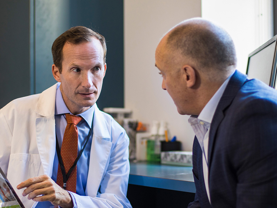 Physician talking with an adult male patient in a clinical office.