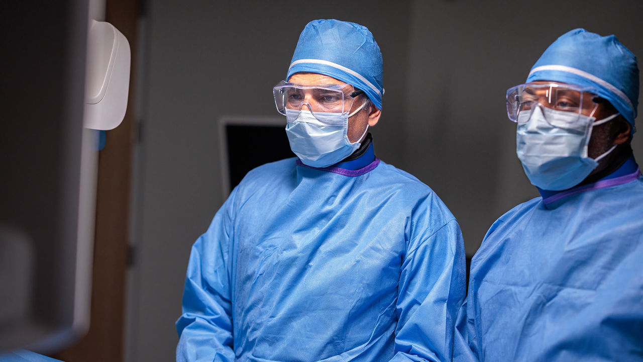 Two surgeons in protective gowns and masks preparing for a benign prostatic hyperplasia (BPH) procedure in the operating room.