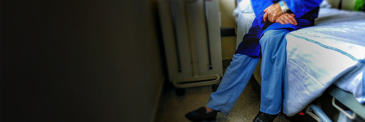 Patient sitting on edge of hospital bed.