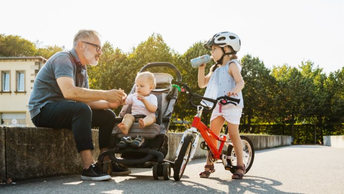  Grandfather sitting on curb with his young grandchildren in stroller and on bike