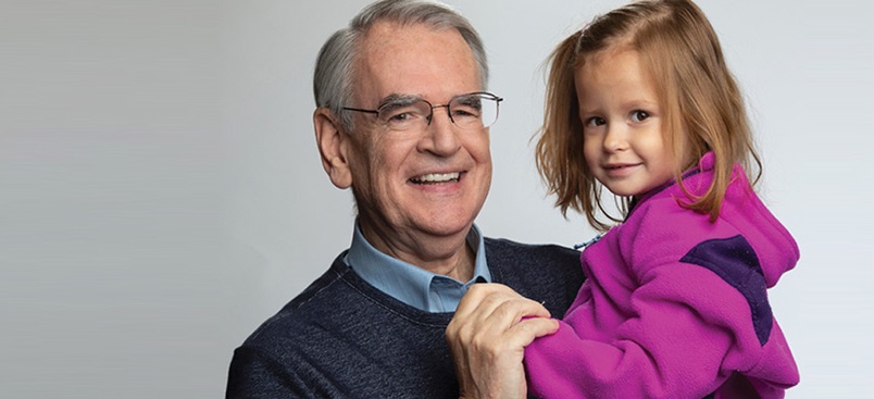 Older man smiling and holding granddaughter 