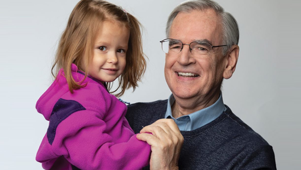 Older man smiling and holding his granddaughter 