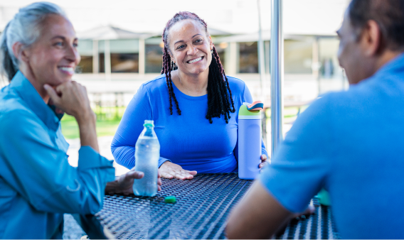 Three people smiling while sitting at an outdoor table with water bottles.