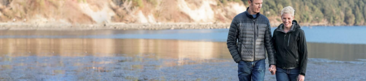 Two people walking hand in hand along a shoreline on a sunny day.