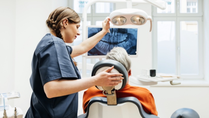 Healthcare provider adjusting light over dental patient with x-ray in background