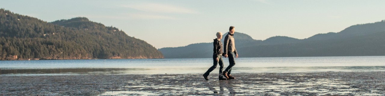 Two people walking along a lake in the sun.