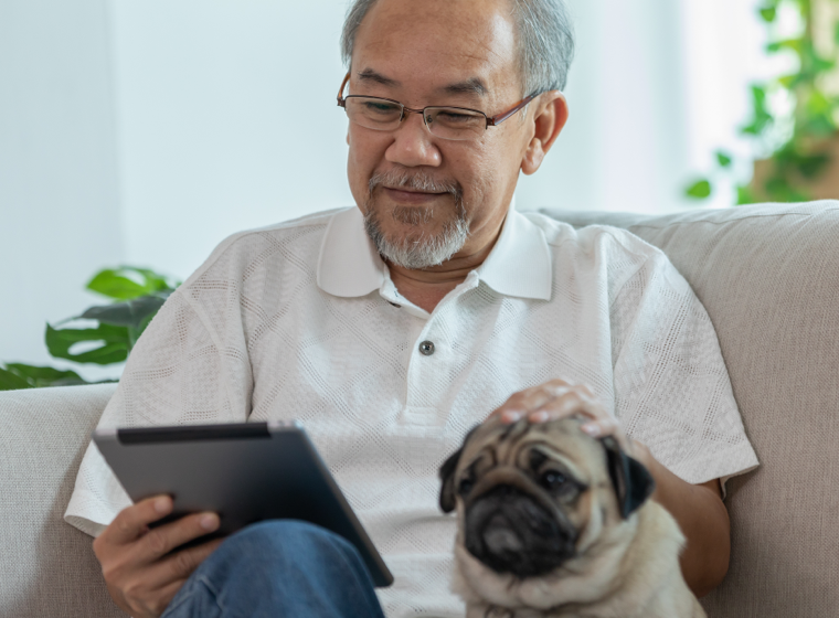 Man smiling and petting his dog while looking at his tablet 