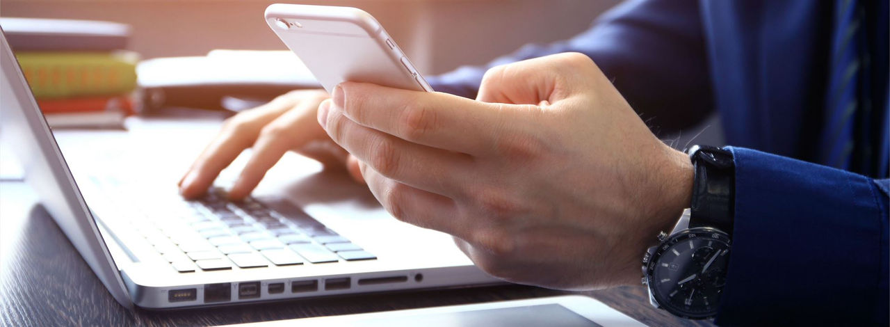 Man holding phone and typing on laptop