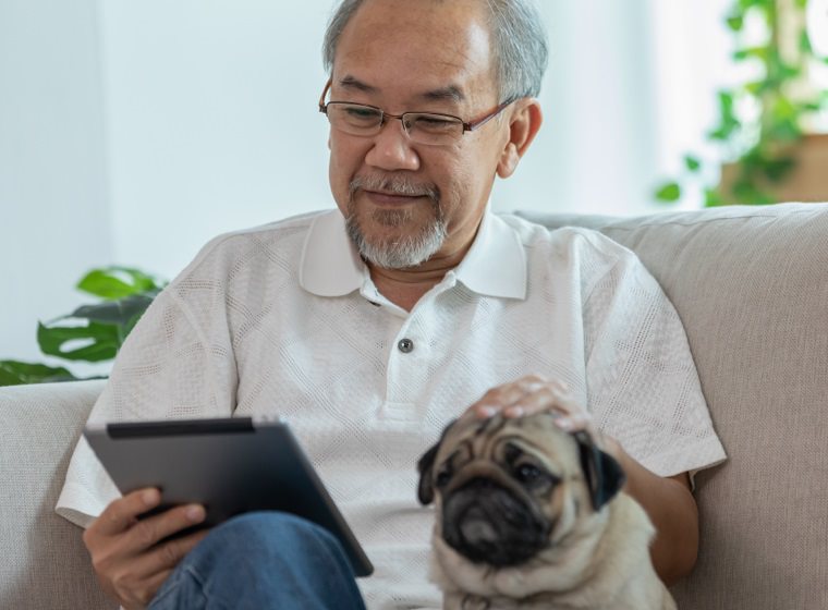 Man smiling while using his tablet and petting his dog