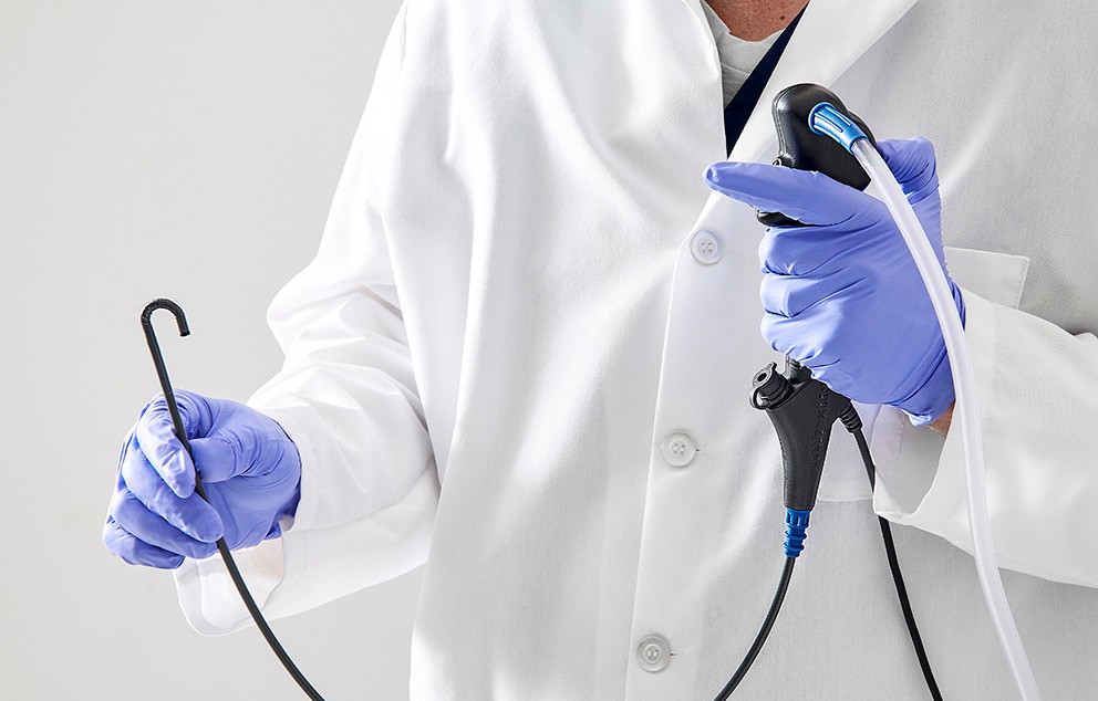 Medical professional in white coat and purple medical gloves handles EXALT Model B Single-Use Bronchoscope.